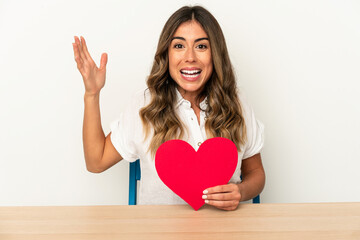 Young caucasian woman holding a valentines day heart isolated receiving a pleasant surprise, excited and raising hands.