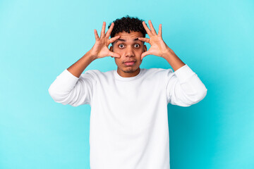 Young african american curly man isolated on blue keeping eyes opened to find a success opportunity.