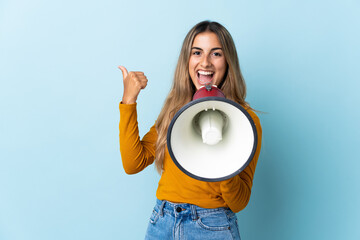 Young hispanic woman over isolated blue background shouting through a megaphone and pointing side