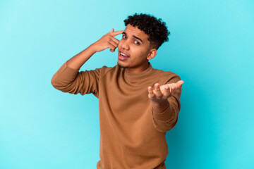 Naklejka premium Young african american curly man isolated on blue holding and showing a product on hand.