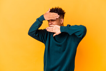 Young african american curly man isolated on purple blink at the camera through fingers, embarrassed covering face.