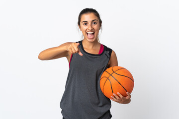 Young hispanic woman playing basketball over isolated white background surprised and pointing front