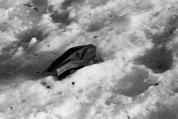 A disposable black medical mask thrown into the snow.