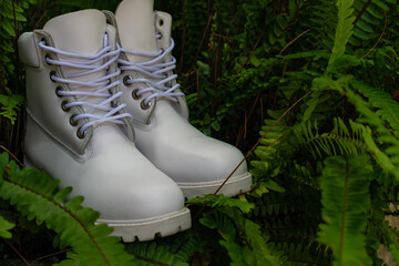 Close-up of a pair of all-white boots, with a low platform sole, surrounded by green vegetation
