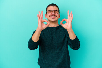 Young caucasian man isolated on blue background cheerful and confident showing ok gesture.