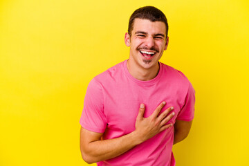 Young caucasian cool man isolated on yellow background laughs out loudly keeping hand on chest.