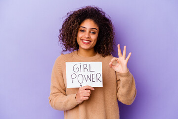 Young African American woman holding a Girl power placard isolated on purple background cheerful...