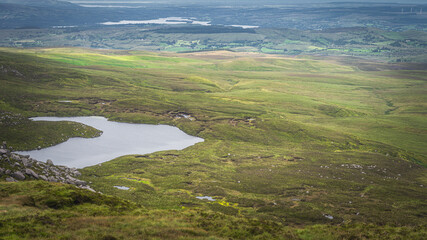 View from Cuilcagh Mountain on lakes, green meadows and fields with patches of sunlight in the valley below, Northern Ireland