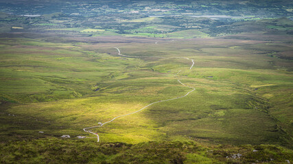 View from the mountain peak on winding wooden path of Cuilcagh Park boardwalk illuminated by sunlight in the valley below, Northern Ireland