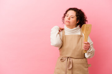 Woman with Down syndrome cooking at home isolated on pink background touching back of head, thinking and making a choice.