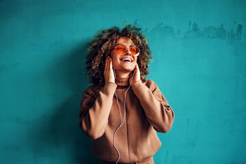 Portrait of fashionable smiling young woman with curly hair listening to the music and looking away.