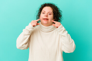 Woman with Down syndrome isolated smiles, pointing fingers at mouth.