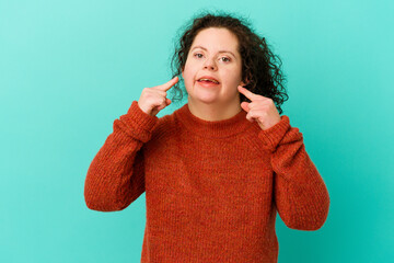 Woman with Down syndrome isolated smiles, pointing fingers at mouth.