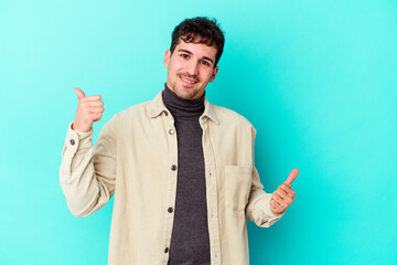 Young caucasian man isolated on blue background raising both thumbs up, smiling and confident.