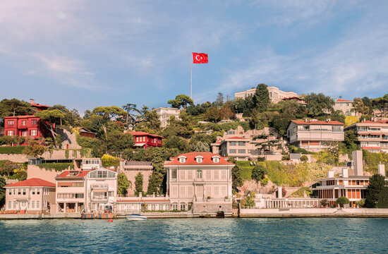 View from the waters of Bosporus Strait on hilly residential blocks of Kandilli neighborhood with red Turkish flag soaring in the sky above Uskudar district of Istanbul