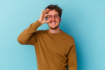 Young caucasian man wearing eyeglasses isolated on blue background excited keeping ok gesture on eye.