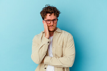 Young caucasian man wearing eyeglasses isolated on blue background blows cheeks, has tired expression. Facial expression concept.