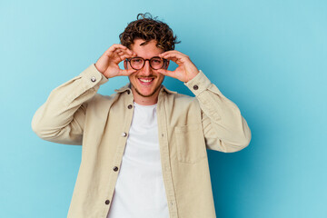 Young caucasian man wearing eyeglasses isolated on blue background showing okay sign over eyes