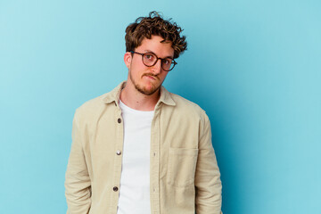 Young caucasian man wearing eyeglasses isolated on blue background shrugs shoulders and open eyes confused.