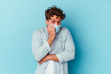 Young caucasian man wearing an antiviral mask isolated on blue background biting fingernails, nervous and very anxious.