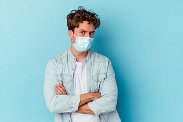 Young caucasian man wearing an antiviral mask isolated on blue background unhappy looking in camera with sarcastic expression.