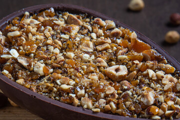 Close up of a stuffed hazelnut and chocolate easter egg on a wooden stand on a wooden table.