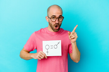 Young caucasian bald man holding a equality gender placard isolated on yellow background having an idea, inspiration concept.