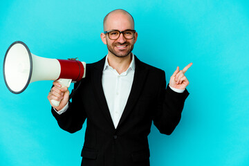 Young business bald man holding a megaphone isolated smiling and pointing aside, showing something at blank space.