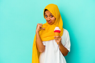 Young muslim woman eating an ice cream isolated on blue background feels proud and self confident, example to follow.