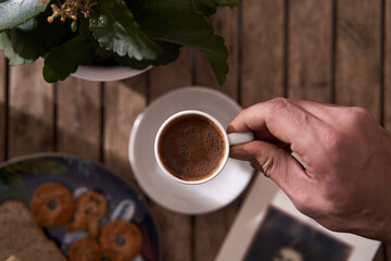 top view, holding coffee cup with wooden background, flowers, books and snacks 