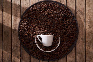 top view, white coffee cup, raw and roasted coffee beans in the dark plate on the wooden table
