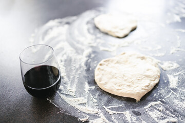 simple food ingredients, pizza dough and flour on kitchen bench ready for homemade pizza next to a glass of red wine