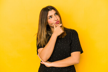 Young indian woman isolated on yellow background thinking and looking up, being reflective, contemplating, having a fantasy.