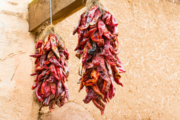 Obraz premium Two bunches of dried hot red chili peppers hanging outside of an adobe building in New Mexico
