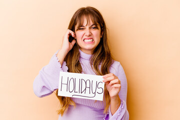 Young caucasian woman holding a Holidays placard isolated covering ears with hands.
