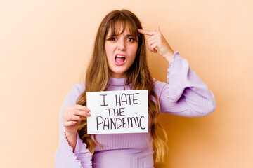Fototapeta na wymiar Young caucasian woman holding a I hate the pandemic placard isolated showing a disappointment gesture with forefinger.