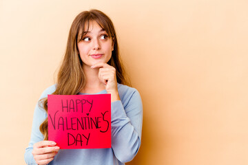 Fototapeta na wymiar Young caucasian woman holding a Happy Valentines day isolated looking sideways with doubtful and skeptical expression.