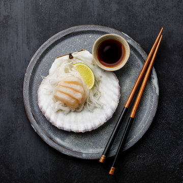 Live scallop sashimi on shell with daikon, lime and soy sauce on dark background