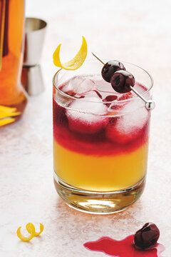 New York Whiskey sour in a glass with ice cubes, cherries on top with syrup and lemon zest garnishes.