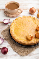 Autumn onion pie and cup of coffee on white wooden background. Side view.