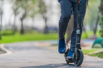 outdoors workout exercise background of man ridding on kick scooter on pavement in park