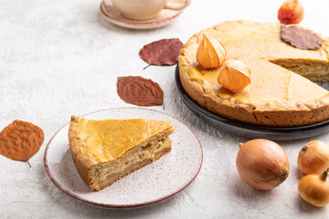 Autumn onion pie decorated with leaves and cup of coffee on gray concrete background. Side view.