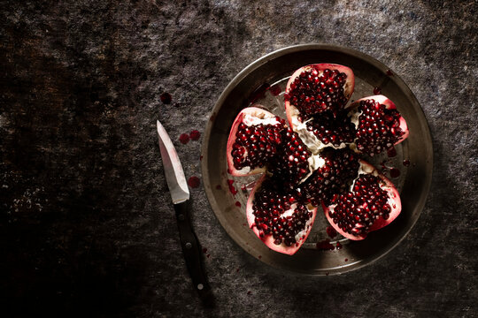 Pomegranate sliced open on a pie plate next to a knife.
