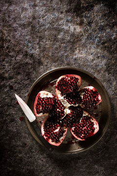 Pomegranate sliced open on a pie plate next to a knife.