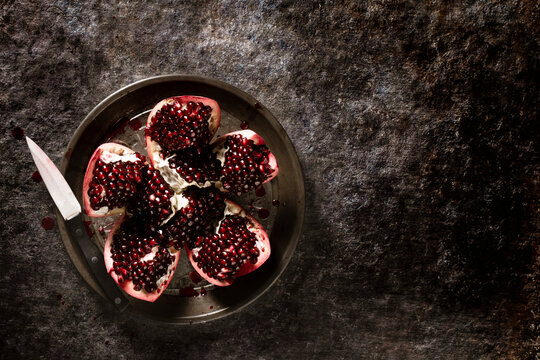 Pomegranate sliced open on a pie plate next to a knife.