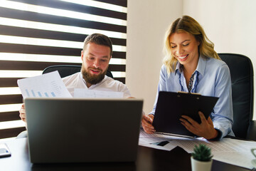 Young caucasian man and woman at office looking project documents analyzing positive reports or contracts having success - happy male and female colleague at work - business and management concept