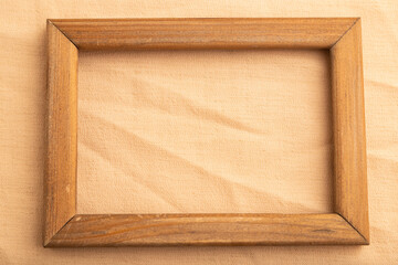 Fototapeta premium Wooden frame on smooth orange linen tissue. Top view, natural textile background.