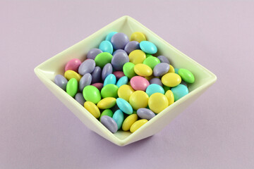 Pastel Easter candy coated milk chocolate candy pieces in white candy dish on lavender background