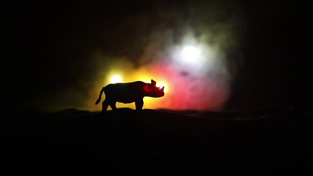 Silhouette of a Rhino miniature standing at foggy night. Creative table decoration with colorful backlight with fog. Selective focus