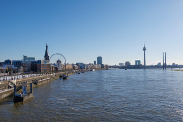 Fototapeta na wymiar Outdoor panoramic sunny scenic cityscape view of Düsseldorf city, Germany, with promenade walkway on waterfront through old town and downtown, view from the bridge over Rhine River in winter. 